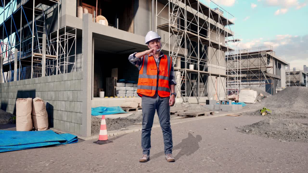 Full Body Of Asian Male Engineer With Safety Helmet Showing Thumbs Down Gesture And Shaking His Head While Standing At Building & Construction Site in Progress to New House