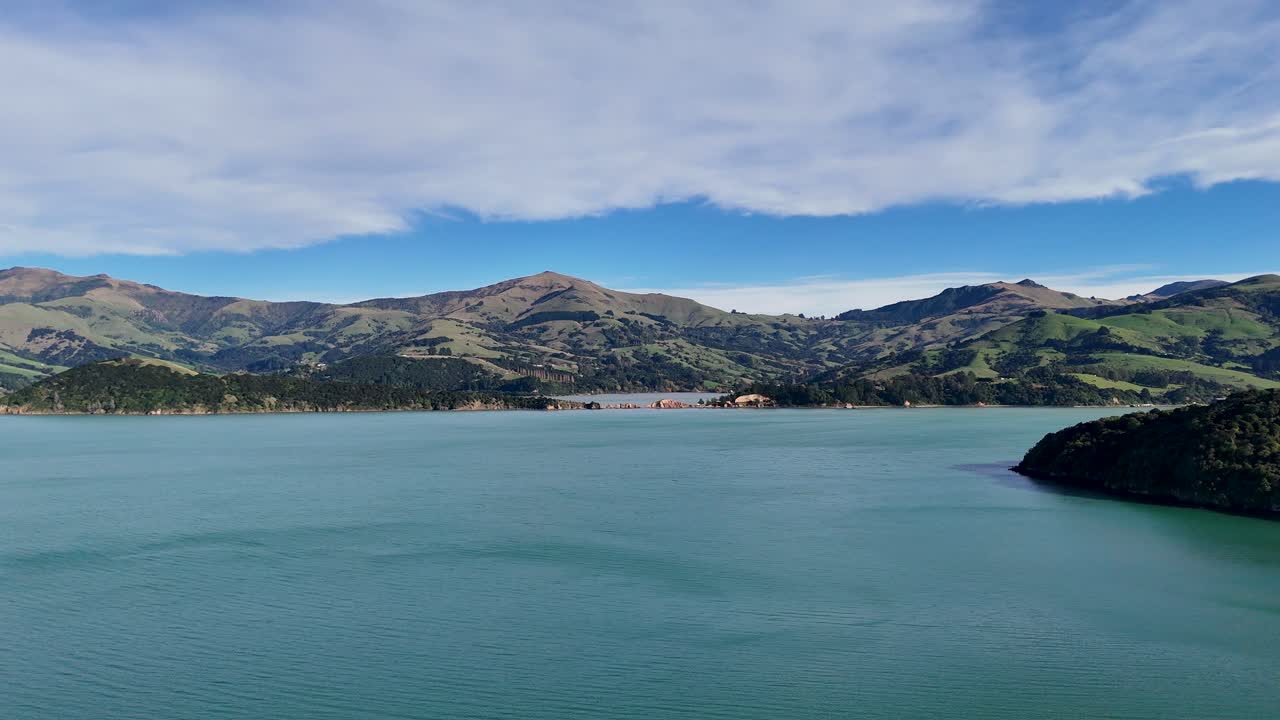 Aerial footage captures Akaroa's serene lake, lush hills, and expansive sky under natural daylight