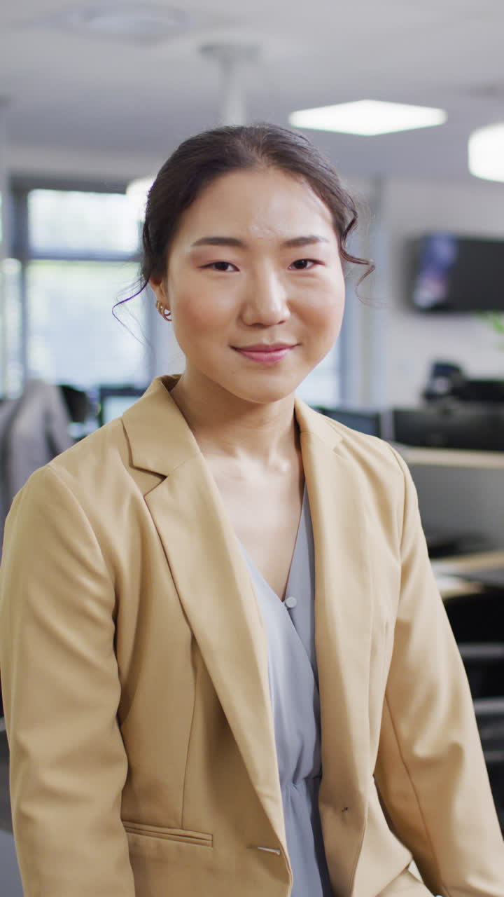 Vertical video of portrait of asian businesswoman looking at camera and smiling at office