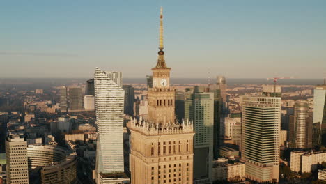 Ziehen-Sie-Den-Schuss-Der-Dekorativen-Spitze-Des-Hohen-Pkin-Gebäudes-Zurück.-Enthüllt-Wolkenkratzer-In-Der-Innenstadt,-Die-Von-Der-Morgensonne-Beleuchtet-Werden.-Warschau,-Polen