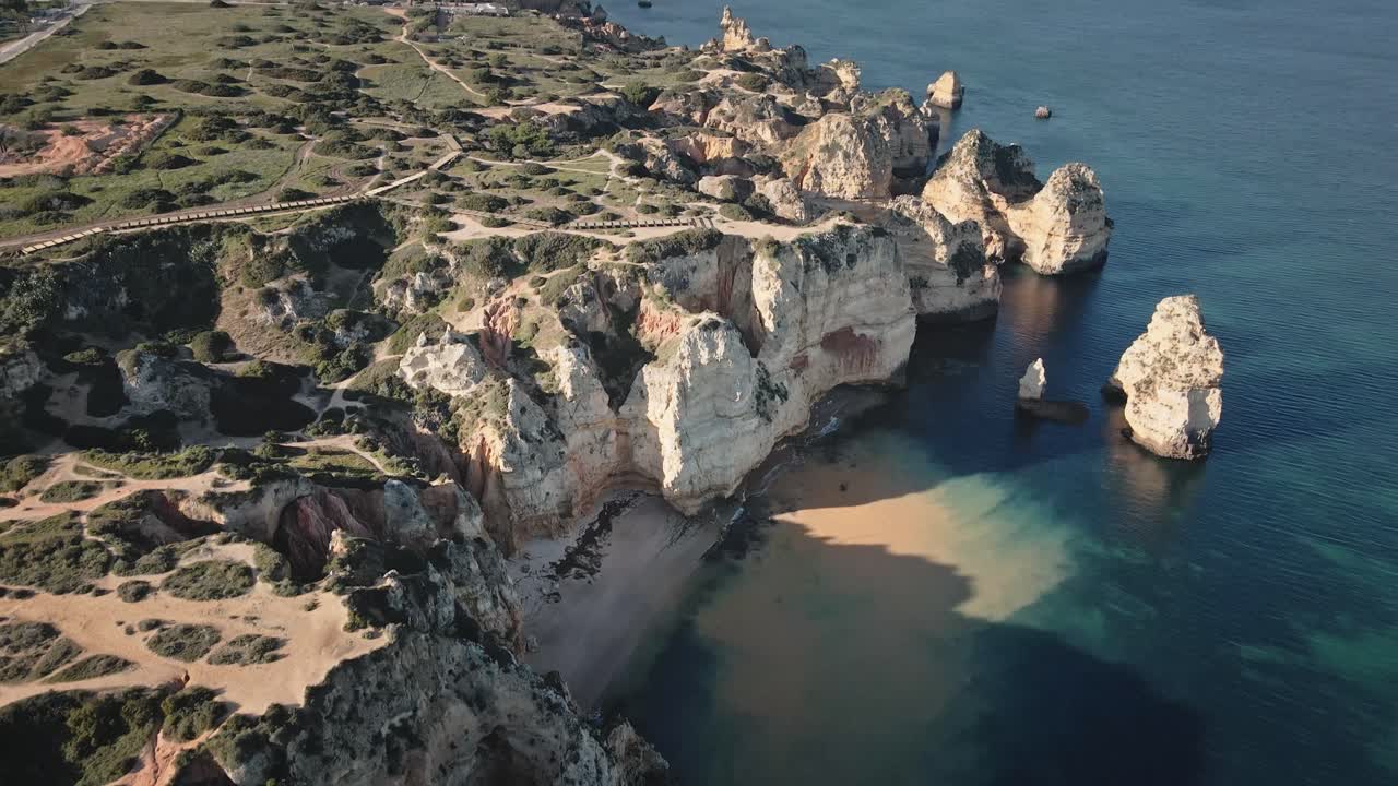 Camera moves forward as it pans upward, unveiling majestic coastal cliffs and turquoise seas before rising to reveal the distant city and skyline
