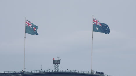 the australian national flag and the state flag of new south wales fly above sydney harbour bridge in sydney, australia - close up, slow motion