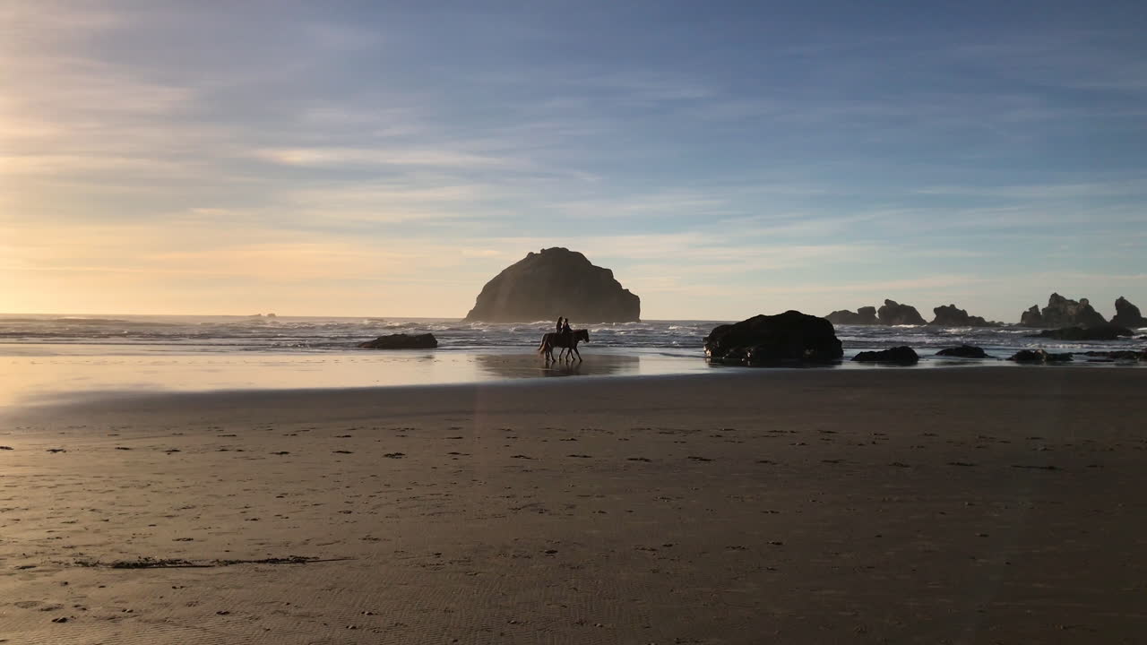 video de silueta en cámara lenta de dos personas montando sus caballos en face rock en bandon, oregon, un parque estatal