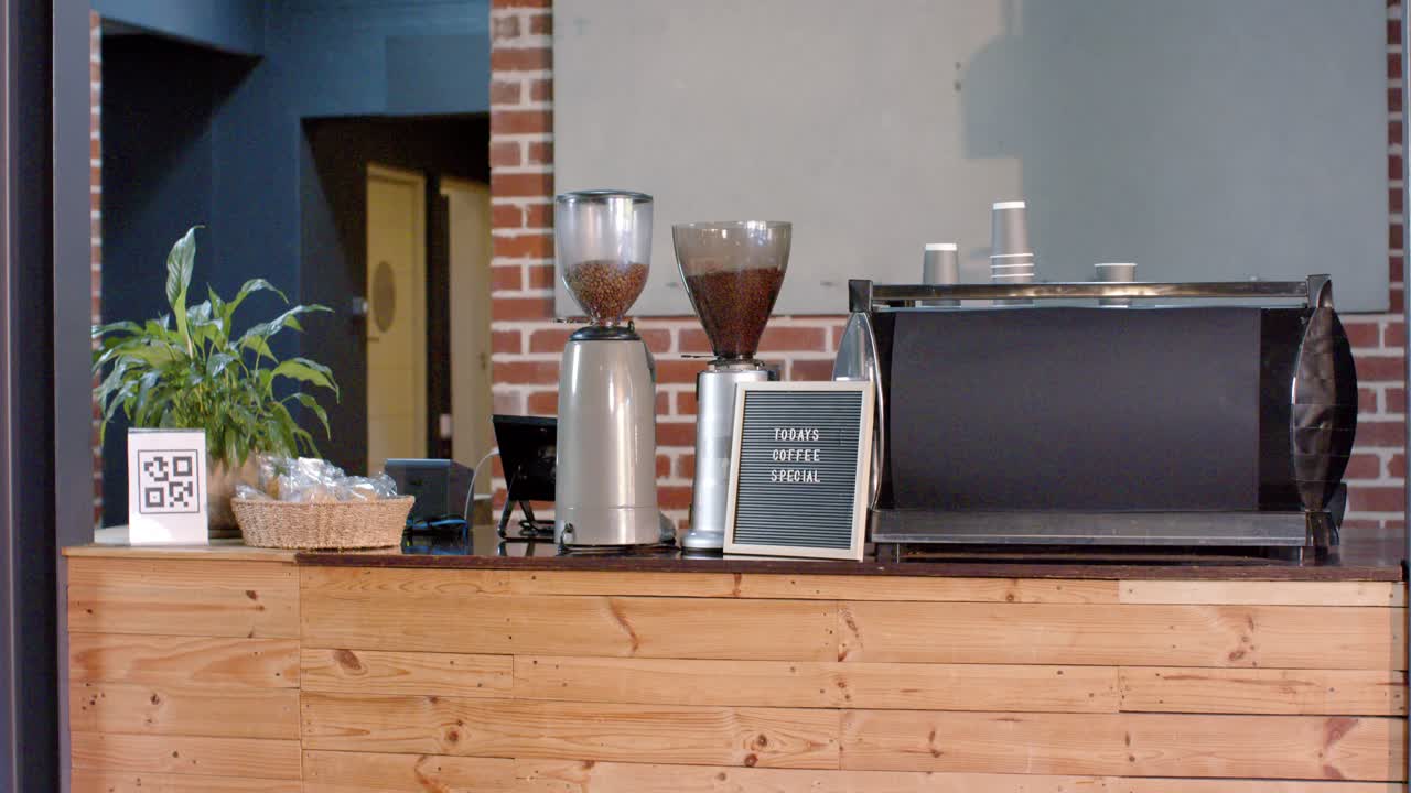 La telecamera esegue una panoramica su un bancone di legno che mostra macinini, una macchina da caffè espresso e un'insegna per presentare il caffè.