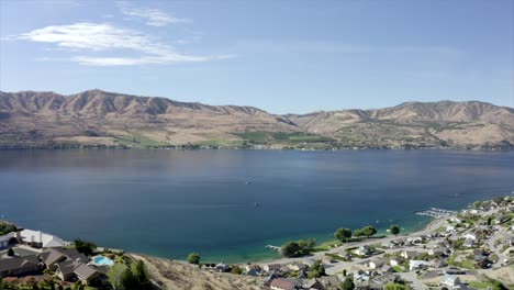 Drone-flying-over-houses-towards-lake-and-mountains