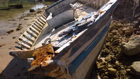 Schiffbrüchiges-Boot-Mit-Blauen-Und-Weißen-Streifen-Am-Felsigen-Strand,-Nahaufnahme-Nach-Links