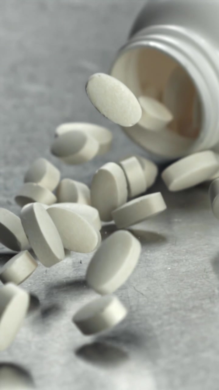 Pillole bianche ovali che cadono da un flacone di medicinali al rallentatore