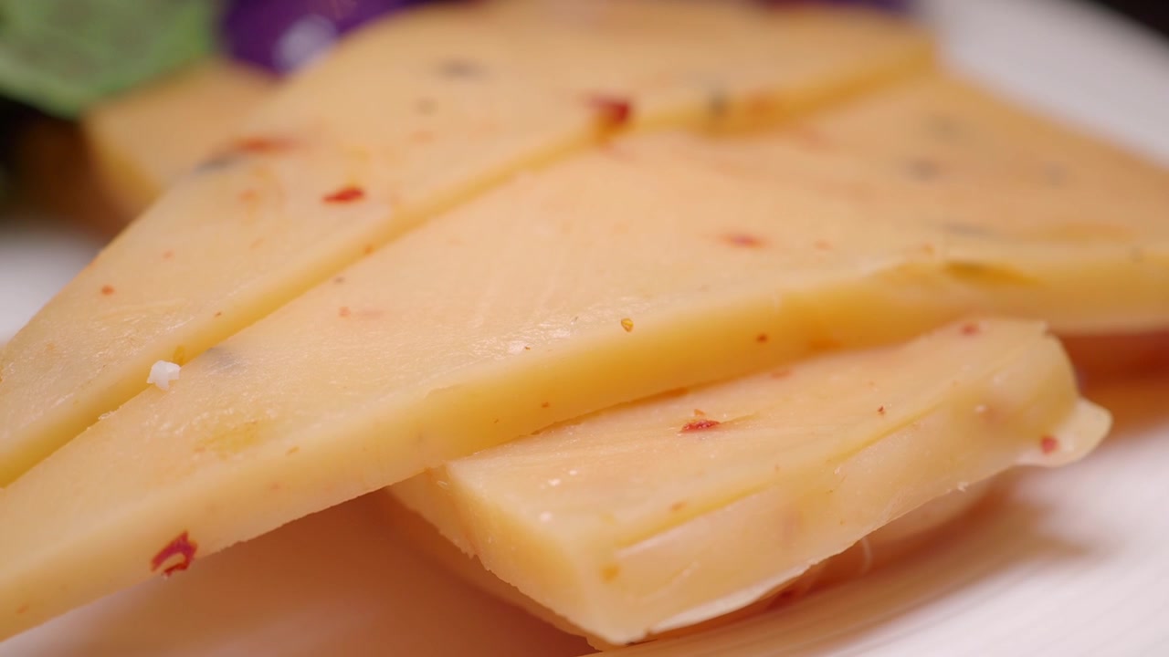 Primer plano de rebanadas de queso triangulares con hojuelas de chile en un plato blanco