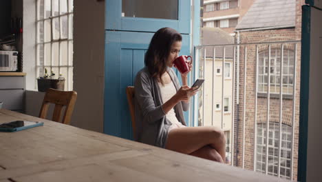 Morning-coffee-for-mixed-race-woman-using-smart-phone-at-home-in-pajamas