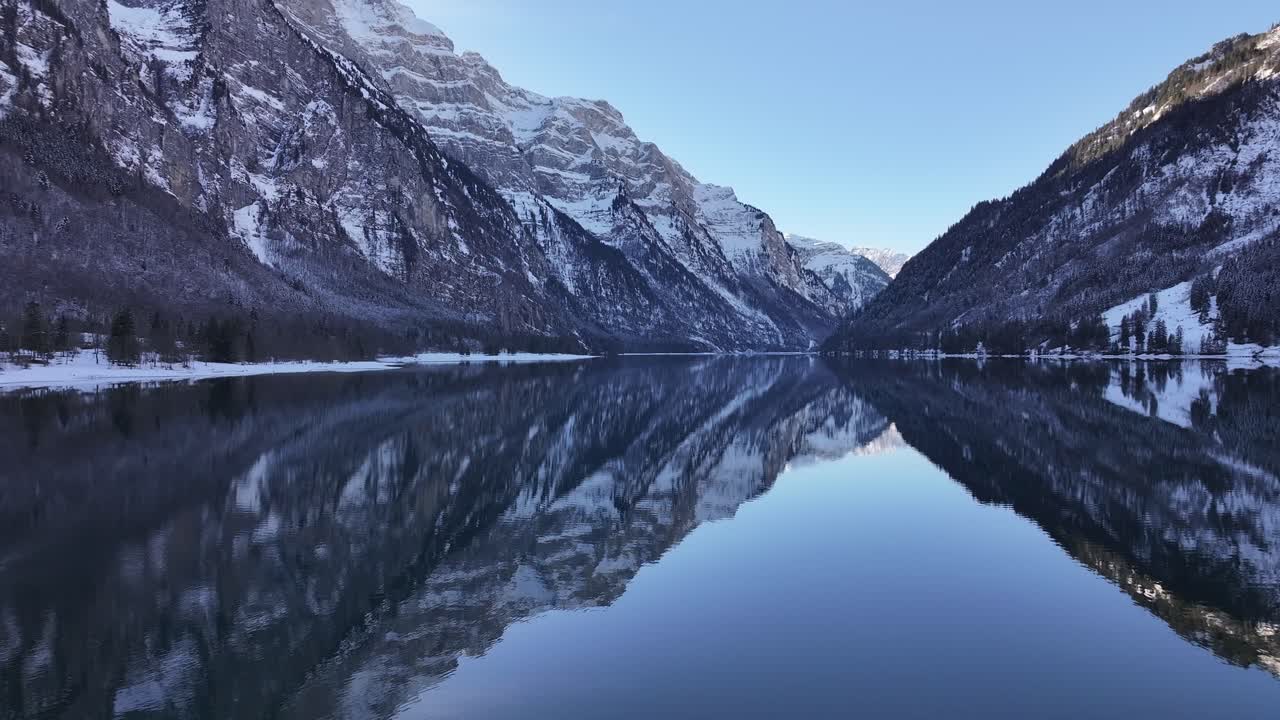 View of the Klöntalersee in Switzerland. The crystal-clear water reflects the snow-capped peaks of the Vorderglärnisch, creating a mesmerizing mirror image.