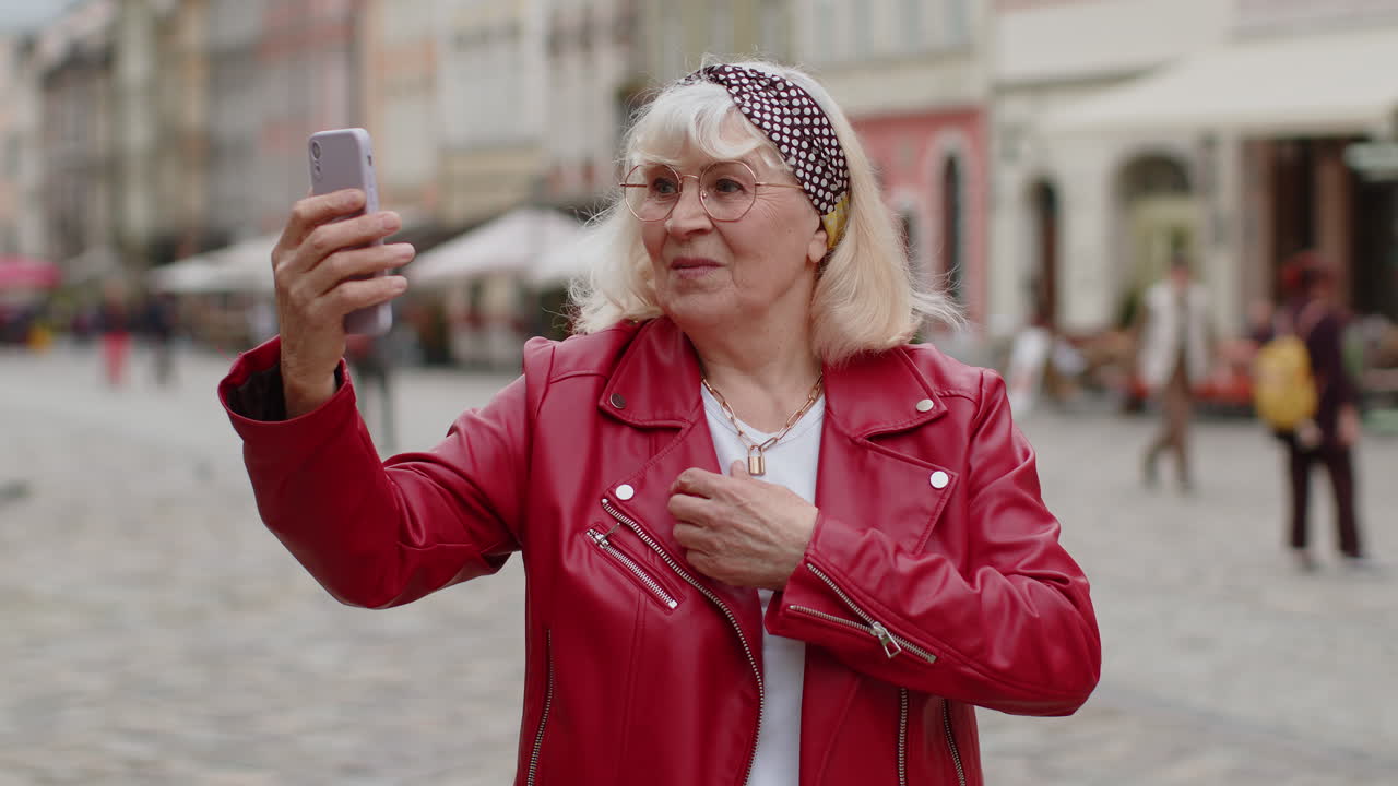 Senior woman blogger taking selfie on smartphone video call online with subscribers in city street