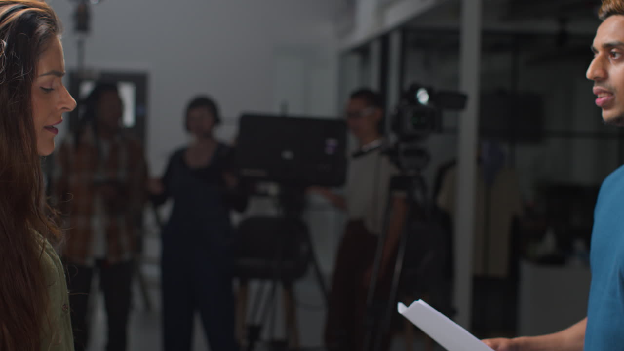 actores con guiones en ensayo rodando una película o video en el estudio con el equipo de filmación y la directora en el fondo
