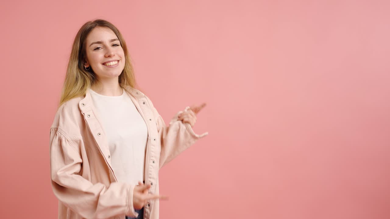 Woman gesturing happily on pink background pointing at space