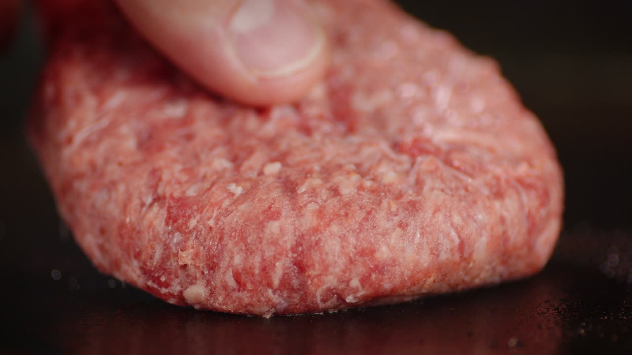 The men's hand puts raw burger meat on a hot frying pan.