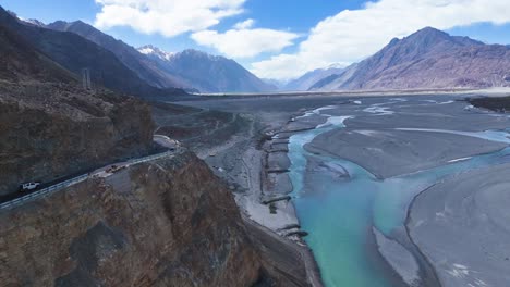 aerial drone shot following a car traveling parallel to the shyok river as it snakes through nubra valley’s landscape.