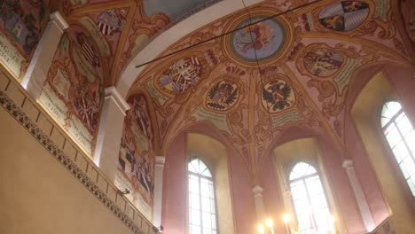 intricate painted ceiling in historic church with heraldic symbols, detailed artwork, and tall arched windows.