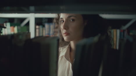 portrait of young thoughtful woman standing behind bookshelf in library