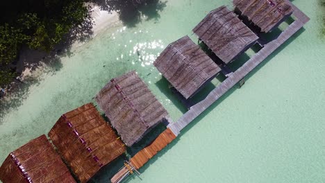 static aerial view above remote, rustic huts overlooking crystal clear ocean water on tropical island in raja ampat, west papua, indonesia