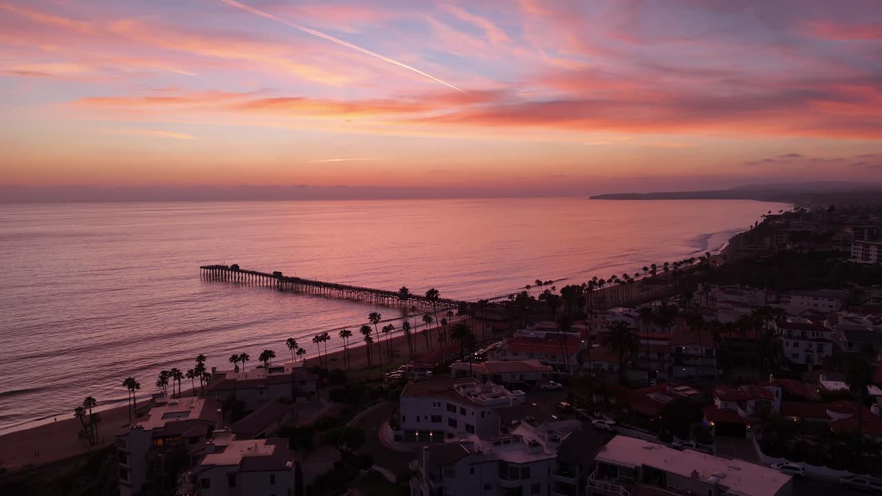 Veduta aerea con drone del Molo di San Clemente al tramonto con soffici nuvole pastello, Oceano Pacifico calmo, spiaggia costeggiata da palme e case lungo la costa a San Clemente, California, Stati Uniti.