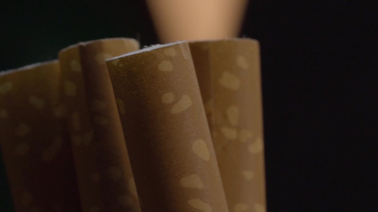 Panning shot moves across brown cigars, revealing natural leaf patterns, smooth rolled surfaces, cylindrical shapes, and fine texture under warm light