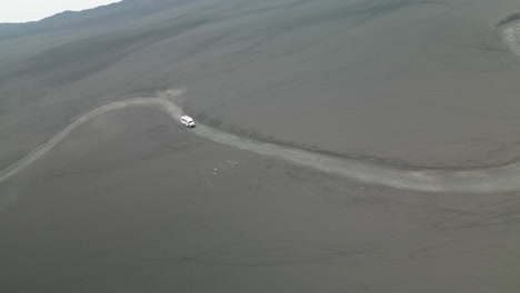 Órbita-Aérea-De-Una-Furgoneta-Blanca-De-Trekking-Que-Conduce-Por-Una-Carretera-Traicionera-Al-Lado-Del-Volcán