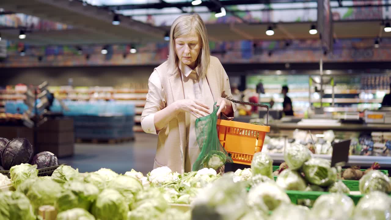 시니어 여성은 채소와 채소를 선택하고 슈퍼마켓에서 생태 가방이나 과일에 넣습니다. 성숙한 여성 고객은 카운터 근처에 식료품 가게를 서 있습니다.