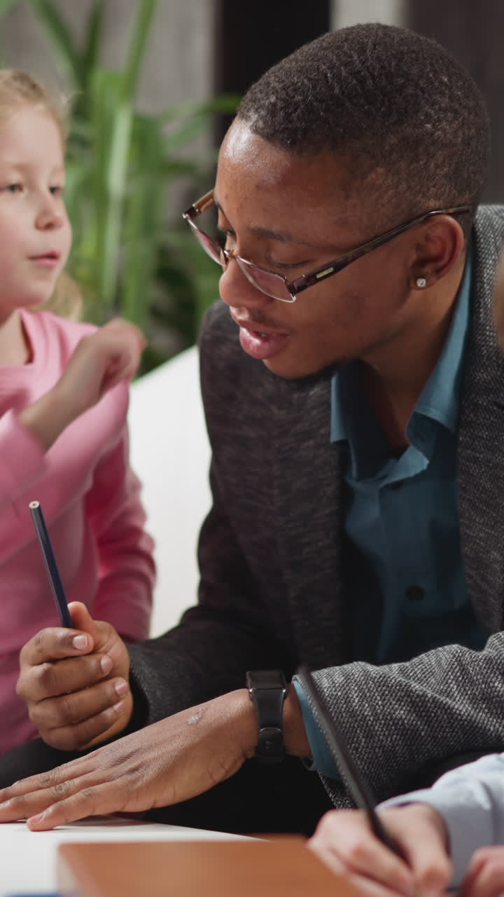 Blonde preschooler girl pupil touches black man teacher ear learning body parts names with brother at private English lesson at home slow motion