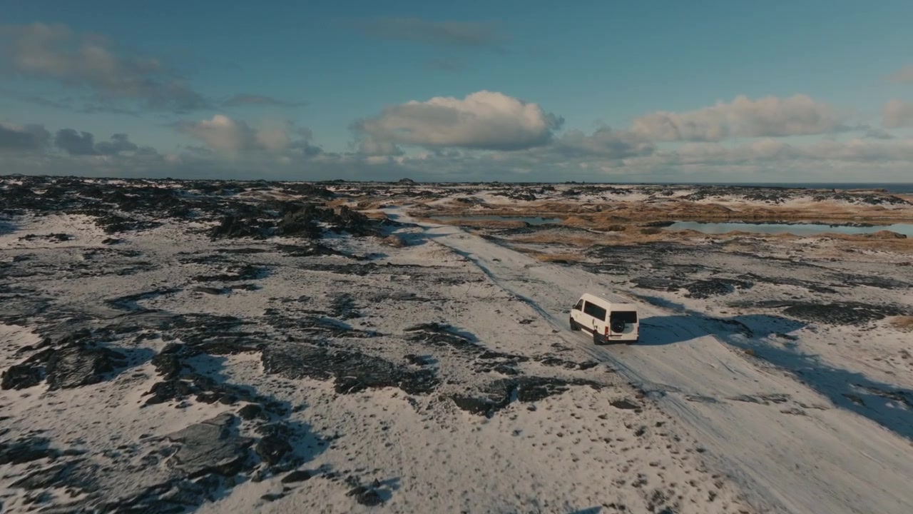 Aerial of Van on Snowy Track Through Lava Field with Ponds