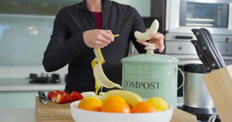 Preparando frutta, una donna con un top nero sbuccia una banana, solleva un coperchio e getta la buccia nel compost in cucina