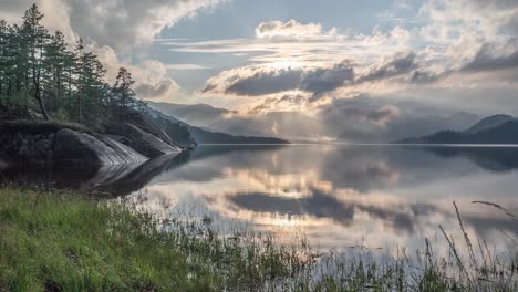 Schwere-Wolken-Im-Gegenlicht-Der-Untergehenden-Sonne-Spiegeln-Sich-Im-Stillen-Wasser-Des-Sees