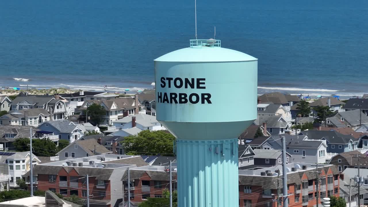 Stone harbor water tower in city with beach houses and waves of Atlantic Ocean. New Jersey state in summer. Aerial orbit shot