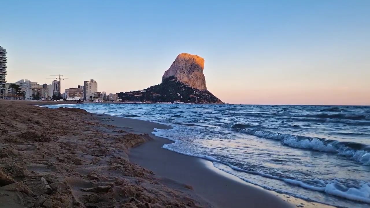 Spiaggia di Calpe con la roccia iconica e il calmo Mar Mediterraneo in Spagna al tramonto
