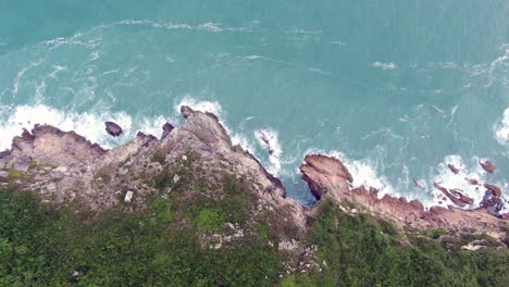 Aerial-view-of-a-jagged-rock-island,-surrounded-with-lush-green-nature-and-Hong-Kong-bay-water