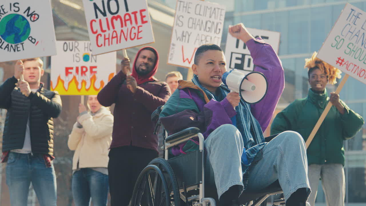 Female Protestor In Wheelchair With Placard And Megaphone On Demonstration Against Climate Change