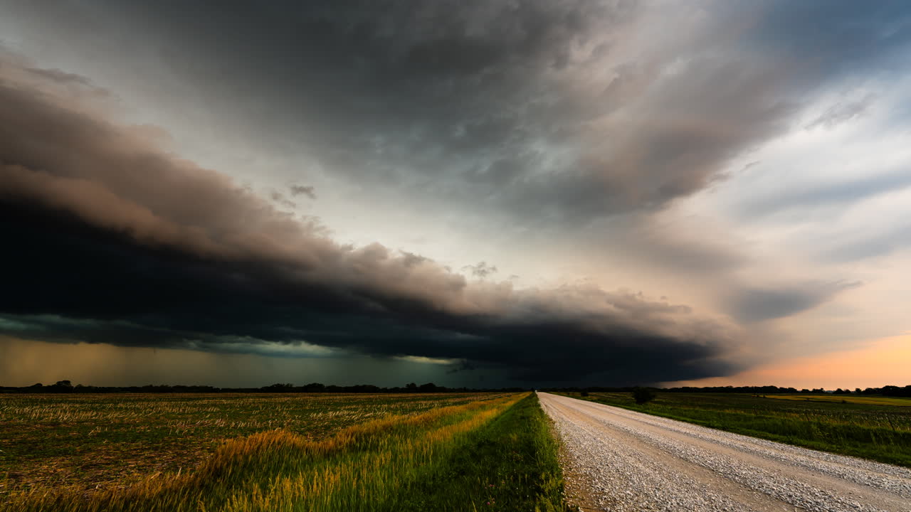 Road leading across fields as colorful storm clouds move overhead