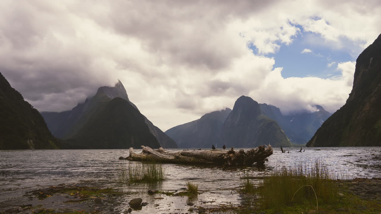 Timelapse image of Milford Sound with drifting clouds over dramatic mountain peaks and reflective water in Fiordland National Park
