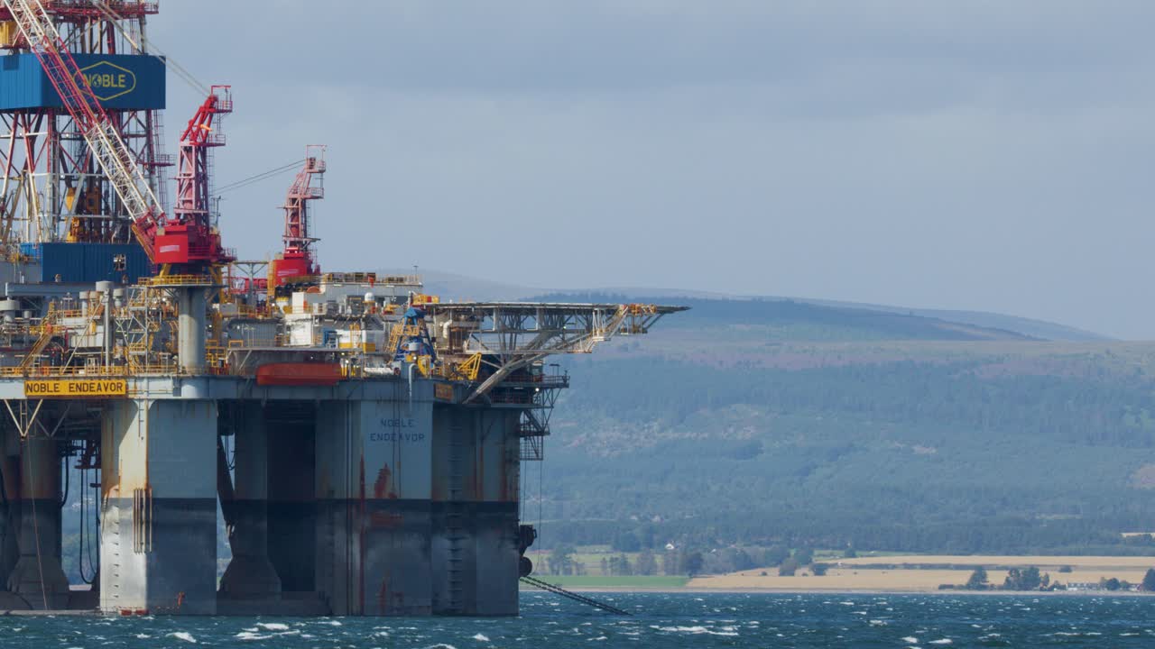 Stor offshore olieplatform med kraner, stationær på roligt hav, fjerne bakker i dagslys