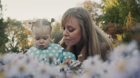 mom and her little daughter are walking in the park, smelling flowers. good time together