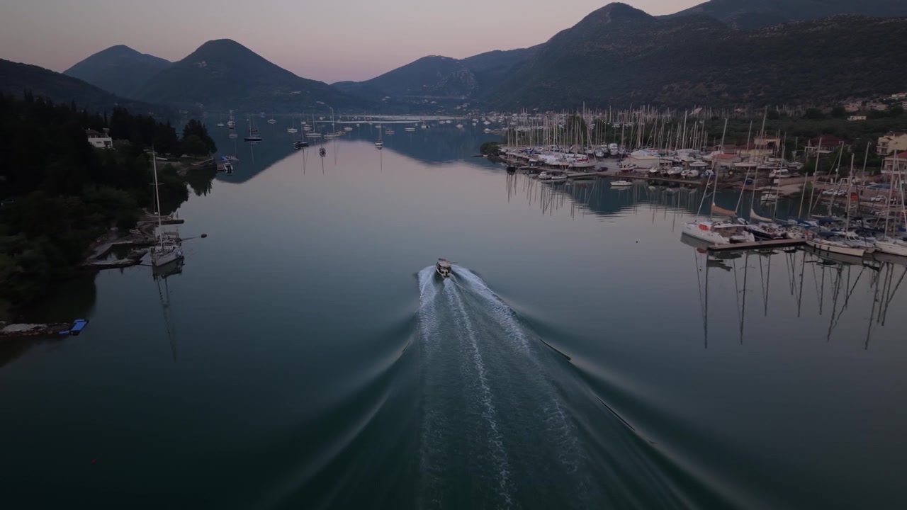 Una barca solitaria naviga su acque calme prima dell'alba a Nidri, Lefkada, lasciando bellissime scie sul mare tranquillo.