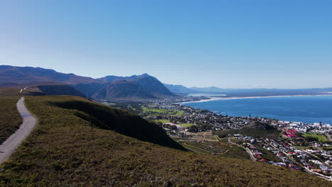 Scenic-aerial-over-mountain-road-with-cyclist-overlooking-Hermanus-and-coastline