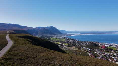 panorámica aérea sobre la carretera de montaña con ciclistas con vistas a hermanus y la costa