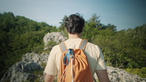 camera tracking a hiker with an orange backpack from behind on a rocky path on mountain sabotin