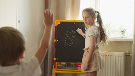 schoolgirl stands at blackboard teaching toddler brother