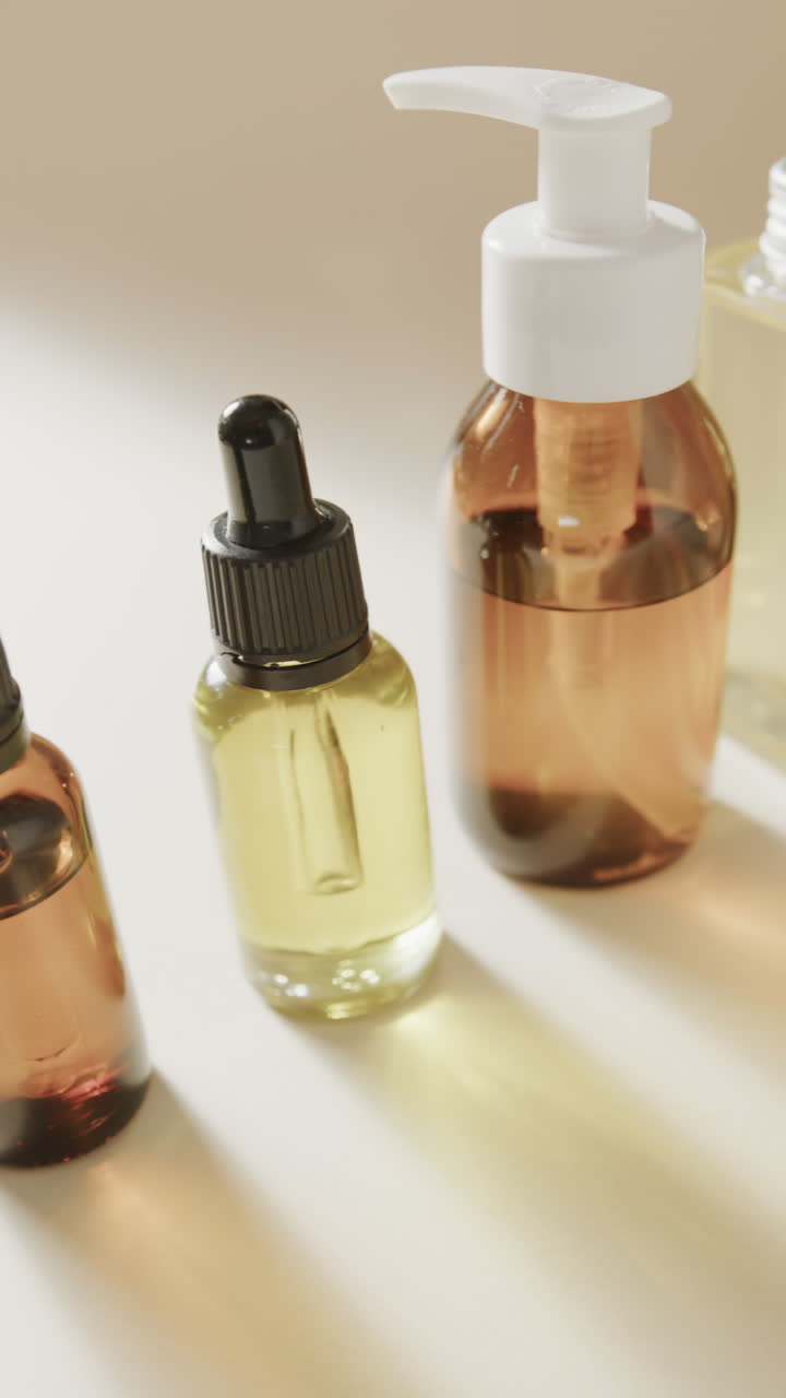 Vertical video of close up of glass bottles with pumps and copy space on beige background