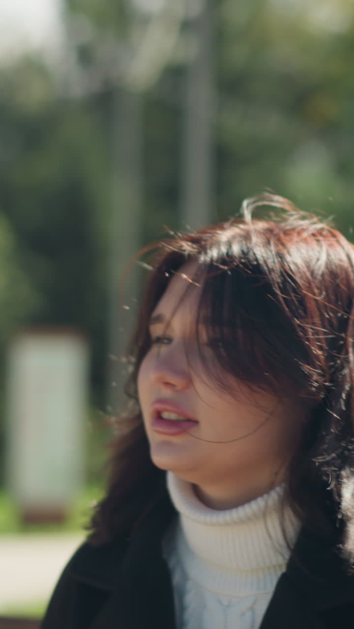 나무로 된 스에 앉아있는 여자의 친밀한 클로즈업, 그녀의 머리카락은 부드럽게 바람에 불어, 울창한 초록색의 조용한 배경