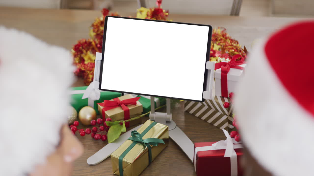 pareja caucásica con sombreros de santa haciendo una llamada de video de tableta con espacio de copia