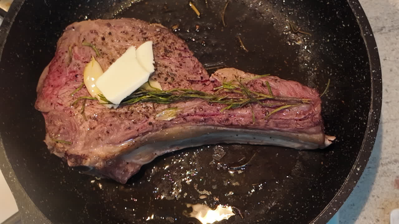 Cooking of a big red beef stake in a black pan with onion and rosemary