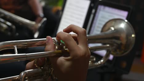 a trumpet moving up and down while fingers pressing the buttons as another trumpet is seen at the background with music piece on the stand, trumpet lesson