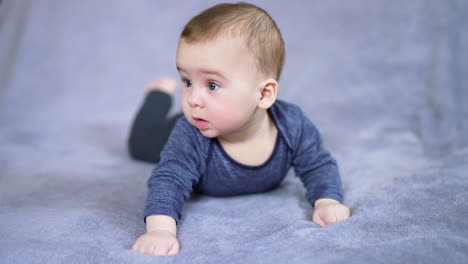 healthy caucasian boy lies on tummy and raises himself on arms. curious toddler looking sideways with interest. grey backdrop.