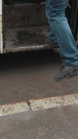 primer plano de dos personas entrando en un autobús blanco estacionado en una carretera mojada. una persona lleva una bolsa negra, y la puerta del autobús se cierra después de la entrada